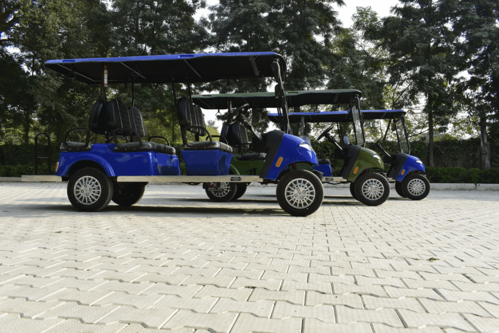 Three six seater golf carts on the concrete ground , front one is blue golf cart, middle is green and the last one is also blue. All 4 forward seat and 2 rear searts