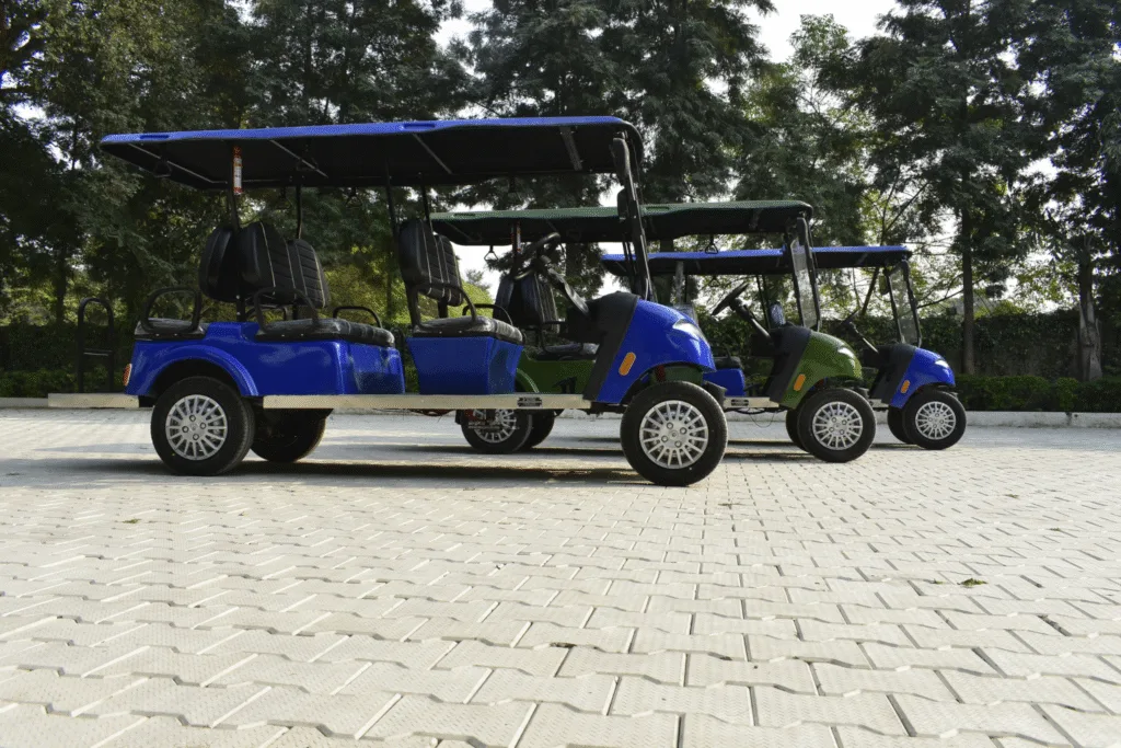 Three six seater golf carts on the concrete ground , front one is blue golf cart, middle is green and the last one is also blue. All 4 forward seat and 2 rear searts